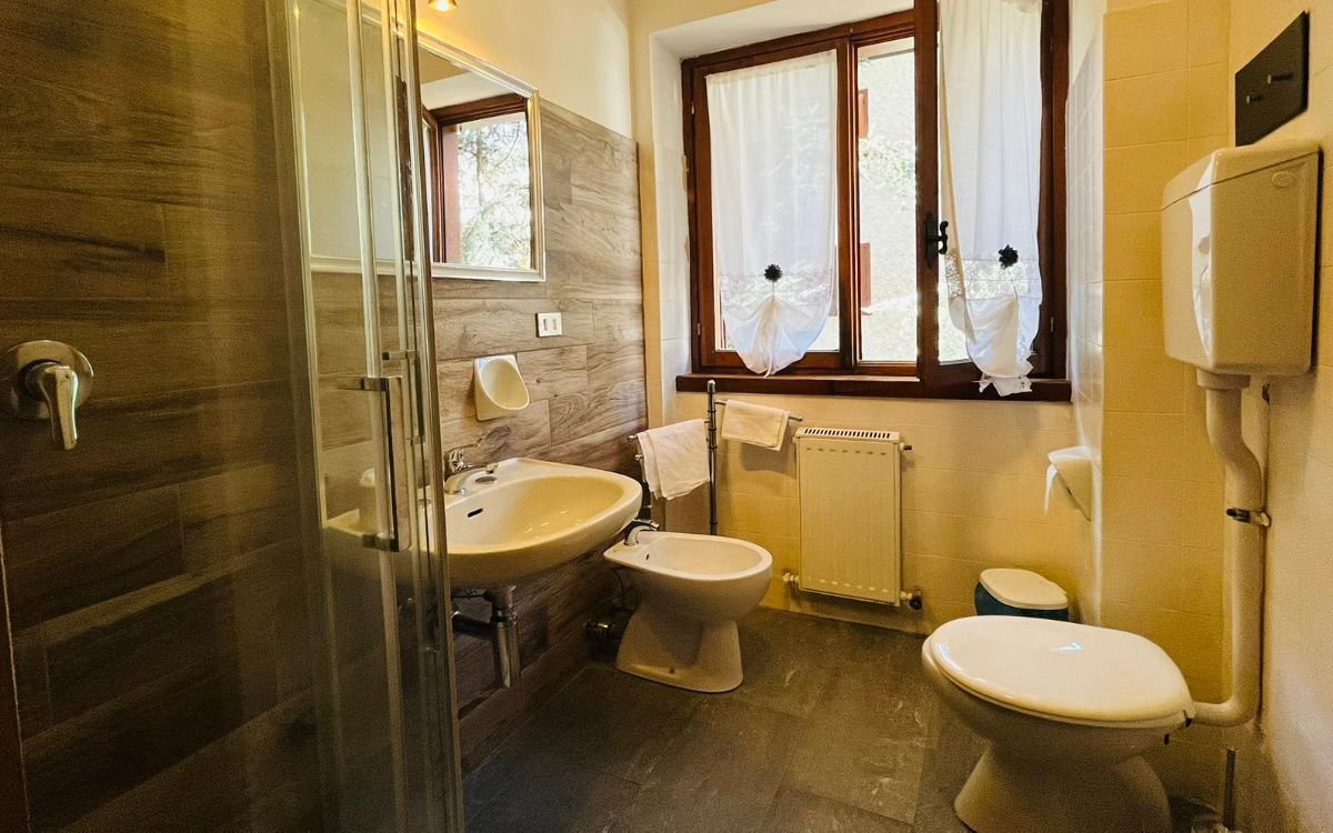 Een badkamer met een douchecabine van glas, een wastafel, een toiletbrons en een toilet.