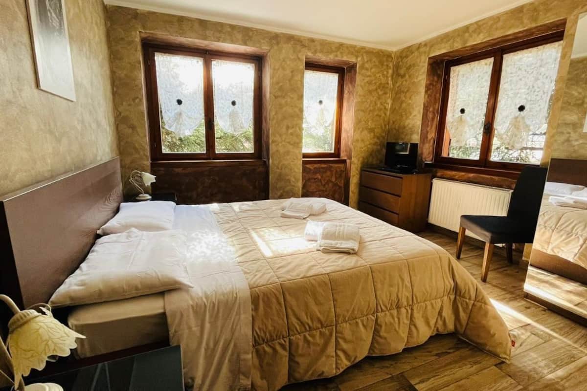 A bedroom with a bed, a desk, a chair, and two windows with curtains.