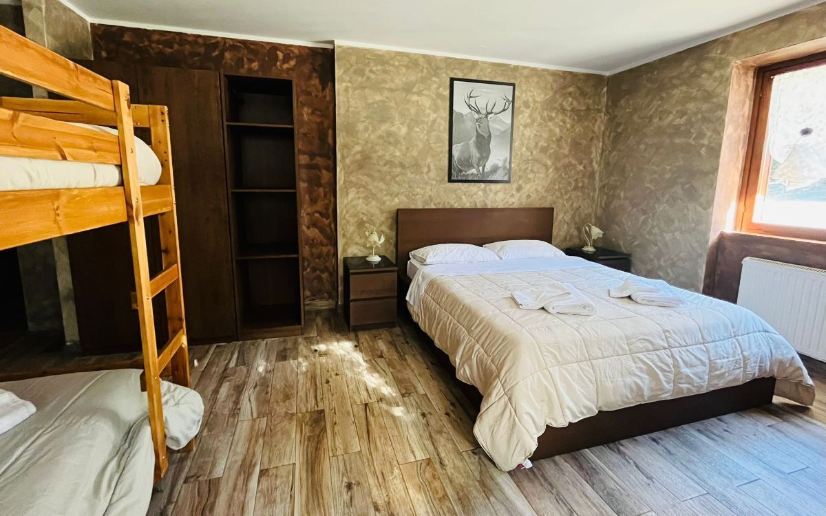 Ein Schlafzimmer mit Etagenbett, Einzelbett, Nachttisch, einem gerahmten Bild und einem Fenster.