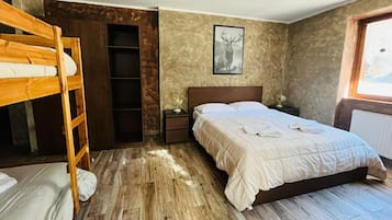 Ein Schlafzimmer mit Etagenbett, Einzelbett, Nachttisch, einem gerahmten Bild und einem Fenster.