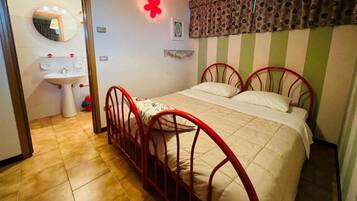 A bedroom with a single bed, a red metal frame, a white bedspread, and a red flower decoration on the wall.