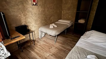 Une pièce avec un lit, une petite table sur laquelle se trouve une télécommande, un tableau accroché au mur et un plancher en bois.