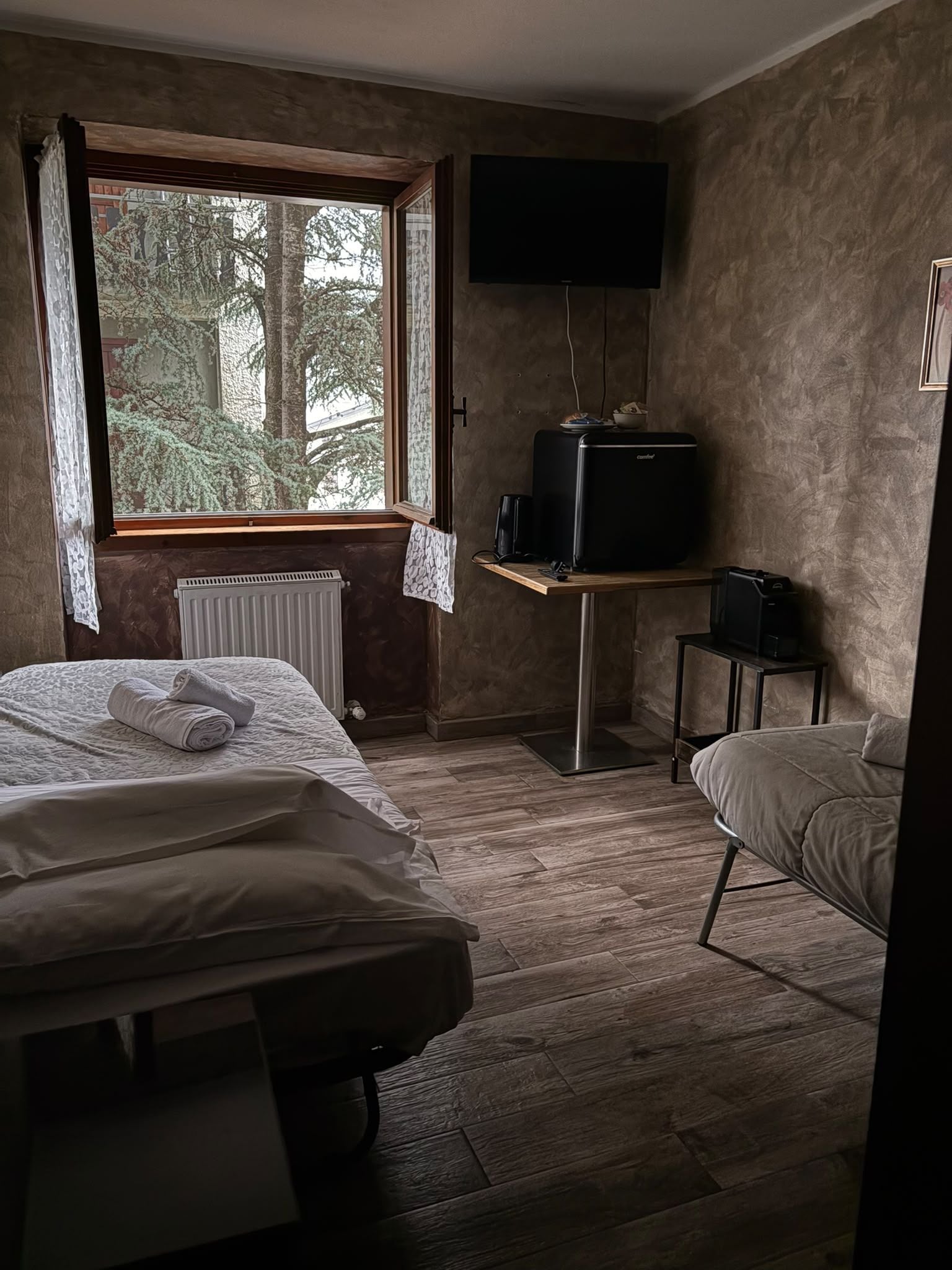 A room with a bed, a chair, a television, and a window with a view of trees.