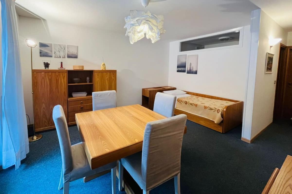 A compact room with a wooden dining table, two chairs, a sofa, and a cabinet.
