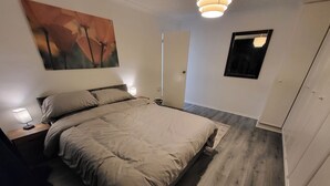 A bedroom with a bed, nightstands, a wall-mounted lamp, a painting, a mirror, and a wardrobe. - Charming 2-bed Apartment in Grays (Grays)