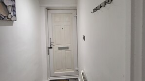 A narrow hallway with a white door at the end, a small rug with a pattern, and a wall-mounted hook. - Charming 2-bed Apartment in Grays (Grays)