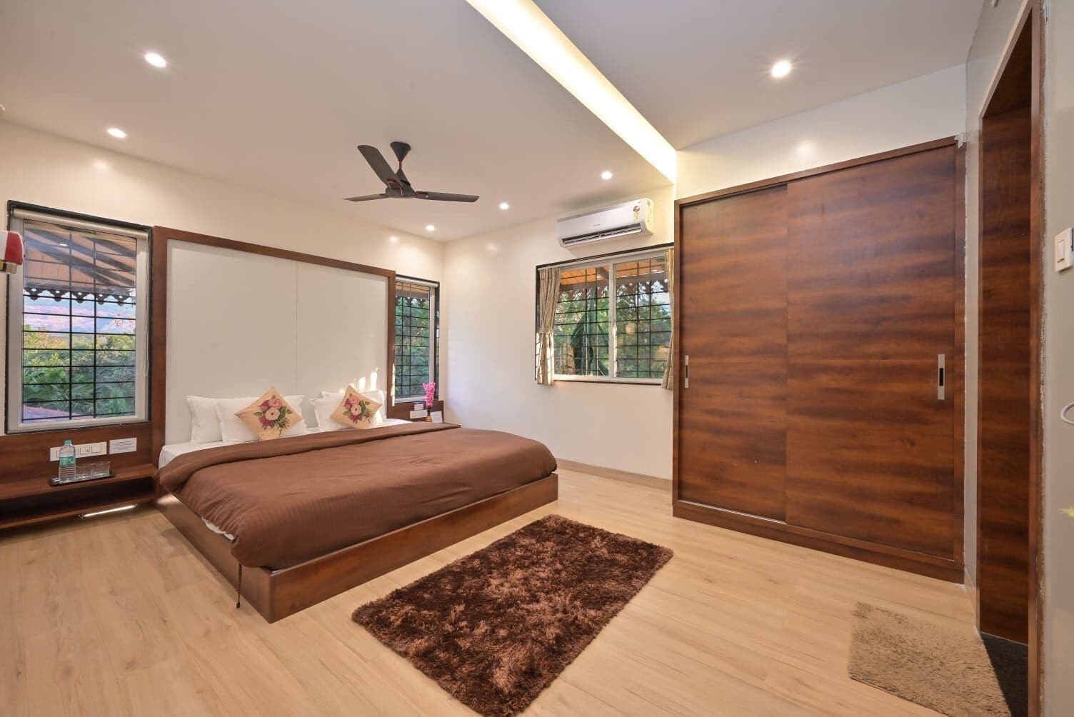 A bedroom with a bed, a ceiling fan, an air conditioning unit, and a wardrobe.
