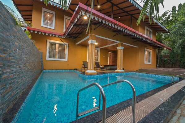 Una piscina con borde de azulejos, un porche cubierto con sillas y un muro de ladrillo.