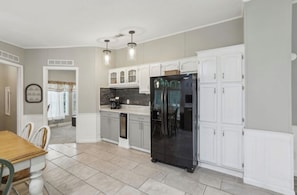 Una cocina con armarios blancos, un refrigerador negro y una zona comedor con mesa y sillas de madera.