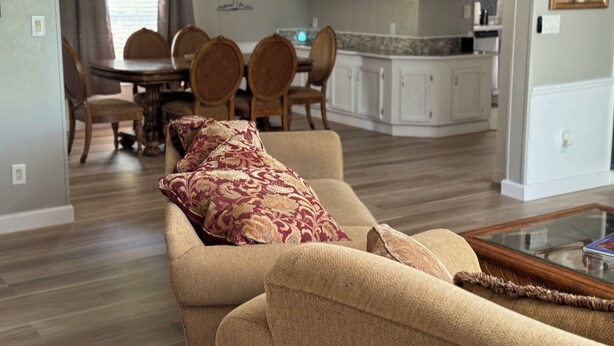 A living room with a beige sofa, patterned cushions, a glass coffee table, and a dining area with a wooden table and chairs. - Florida Woodland Retreat-Nature Coast (Brooksville)