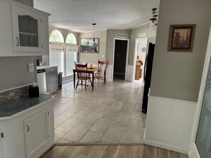A spacious kitchen with a dining area, featuring a large window, a chandelier, and a tiled floor.