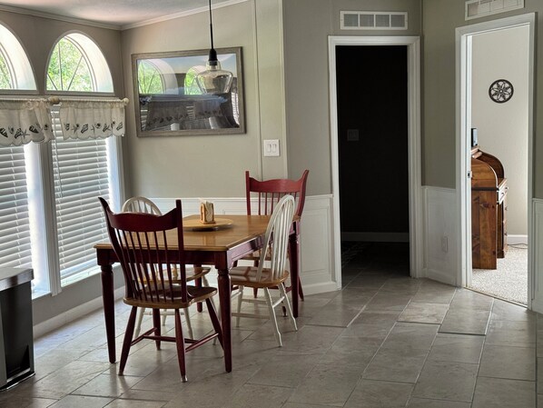A dining area with a wooden table and chairs, a hanging light fixture, and a window with blinds.