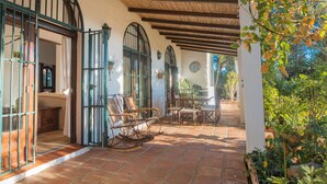 A covered patio with rustic furniture, a clock, and a view of the garden. - Exceptional private villa with sea view & heated pool (Mijas)