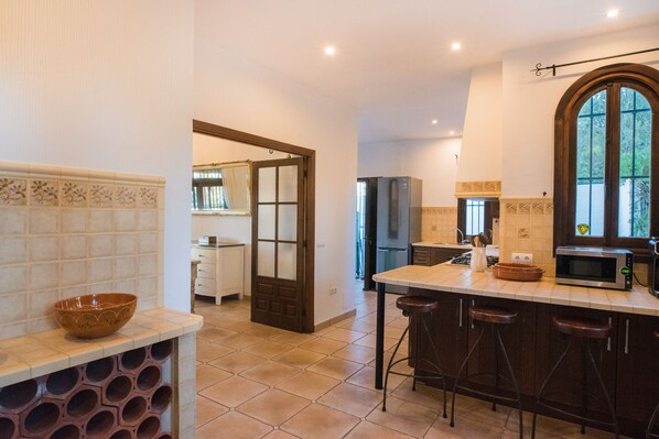 A kitchen with a central island, bar stools, a large window, and a door leading to another room.
