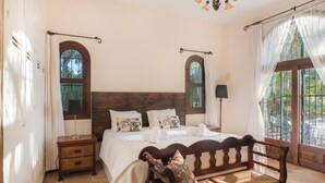 A bedroom with a large bed, two nightstands, a wooden bench, and two windows with curtains. - Exceptional private villa with sea view & heated pool (Mijas)