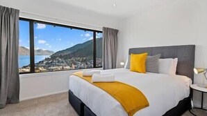 A hotel room with a large bed, a view of a coastal town, and a nightstand with a lamp. - Queenstown Mountain Vista, quick walk to town centre. (Queenstown)