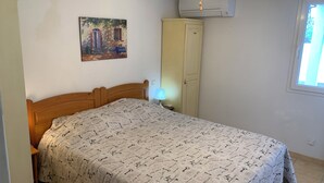 Une chambre à coucher comprenant un lit, une table de chevet, une lampe, un appareil de climatisation, une armoire et une fenêtre.
