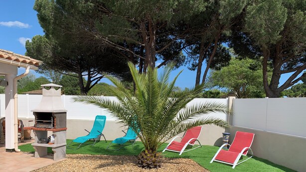Un jardin avec un barbecue, deux fauteuils rouges et un palmier.
