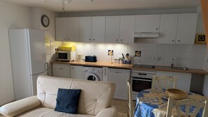 Un espace de vie compact comprenant un coin cuisine, un canapé, une table à manger et un lave-linge.