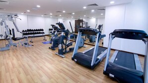 Une salle de sport équipée de tapis de course, d’appareils de musculation et d’un mur entièrement recouvert de miroirs.
