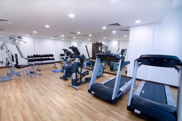 Un gimnasio con cintas de correr, máquinas de pesas y un muro de espejos.