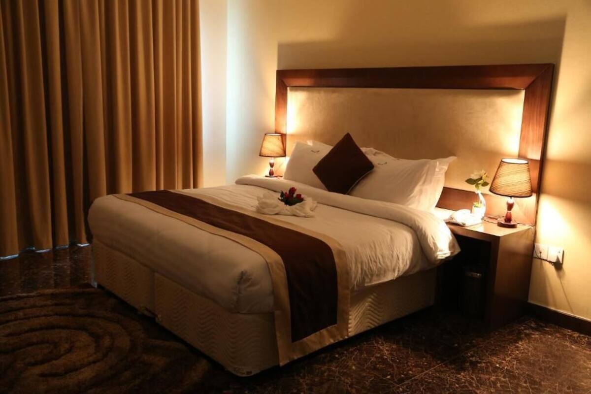 A hotel room with a large bed, two bedside lamps, a wooden headboard, and a brown carpet.