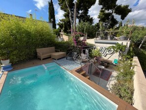 Una piscina con un sillón de sol, una mesita y una zona de estar cubierta.