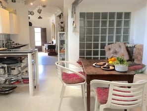 Cozinha moderna com eletrodomésticos de aço inoxidável, sala de jantar com mesa de madeira e cadeiras brancas, e uma grande janela com design em grade.