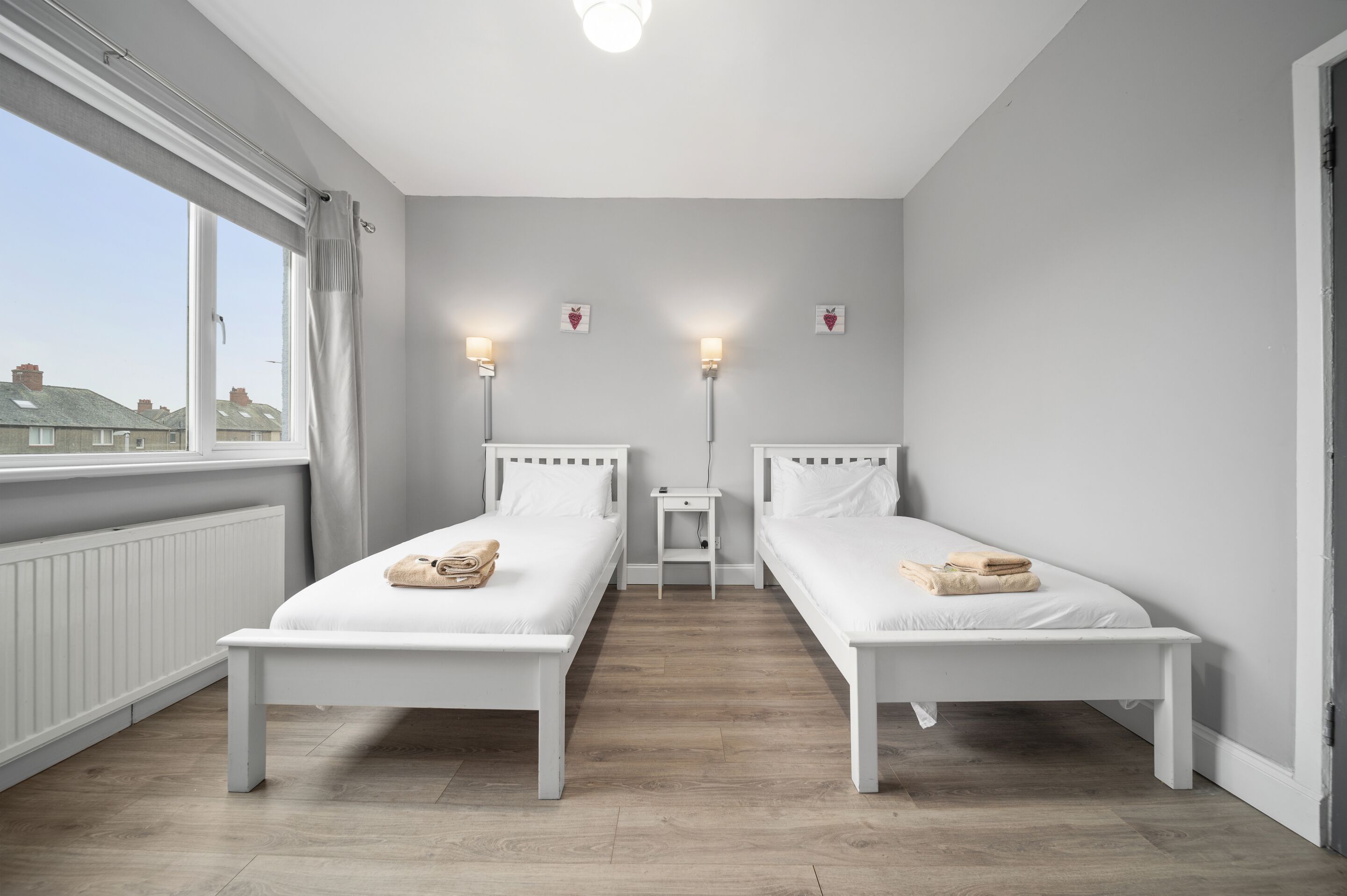 Ein Zimmer mit zwei Einzelbetten, einem kleinen Nachttisch, einem Beistelltisch und einem Fenster mit Vorhängen.