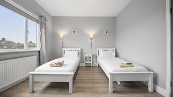 Ein Zimmer mit zwei Einzelbetten, einem kleinen Nachttisch, einem Beistelltisch und einem Fenster mit Vorhängen.