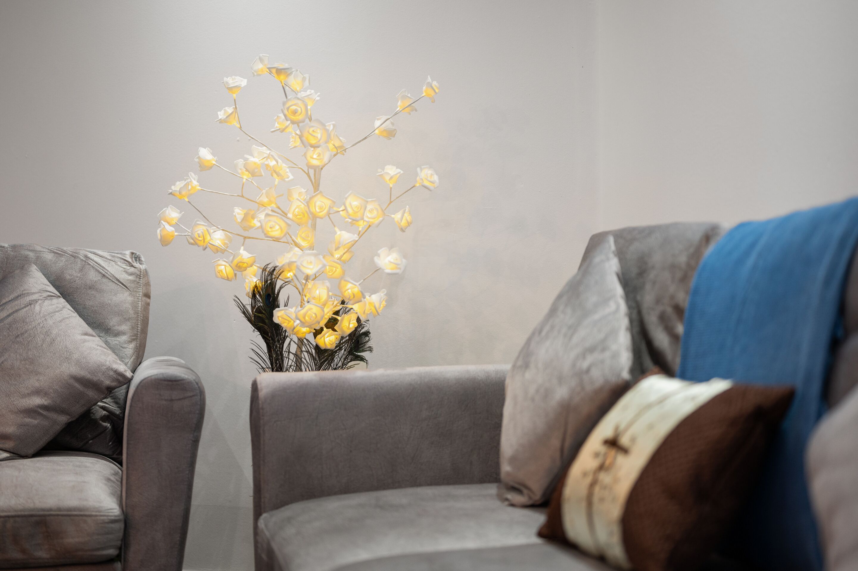 A modern living room with a grey sofa set, a vase with yellow flowers, and a blue throw blanket.