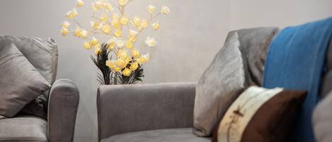 A modern living room with a grey sofa set, a vase with yellow flowers, and a blue throw blanket.