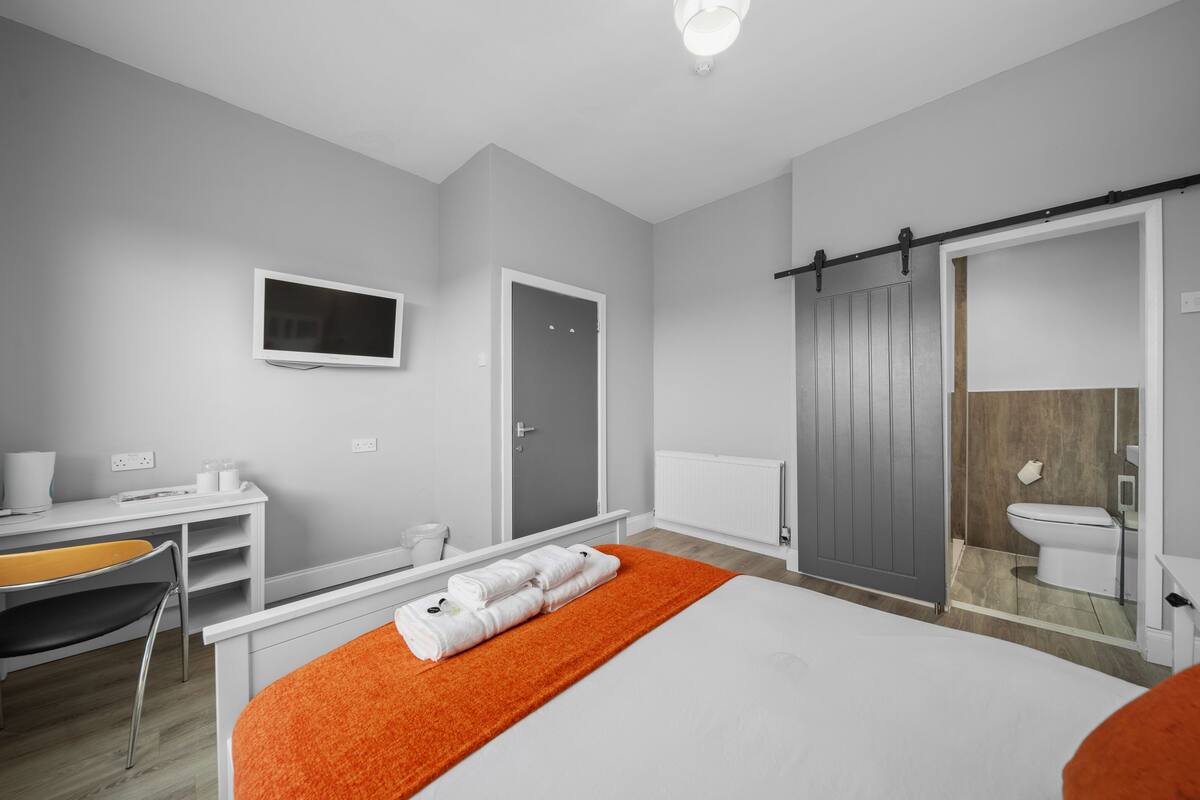 A modern hotel room with a bed, a desk, a chair, a TV, a wardrobe, and a bathroom.