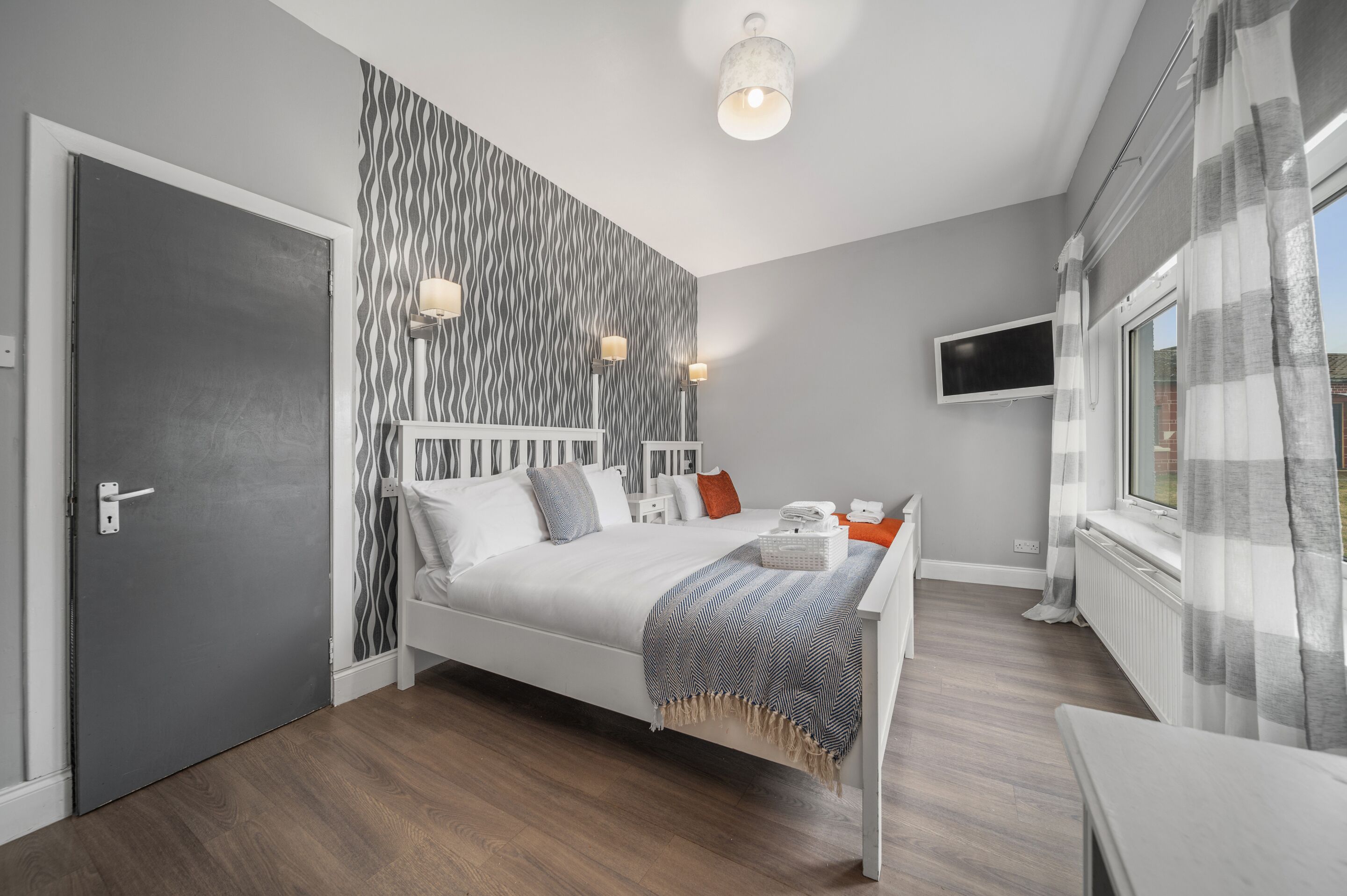 Een moderne slaapkamer met een bed, nachtkastjes, een televisie en een raam met gordijnen.
