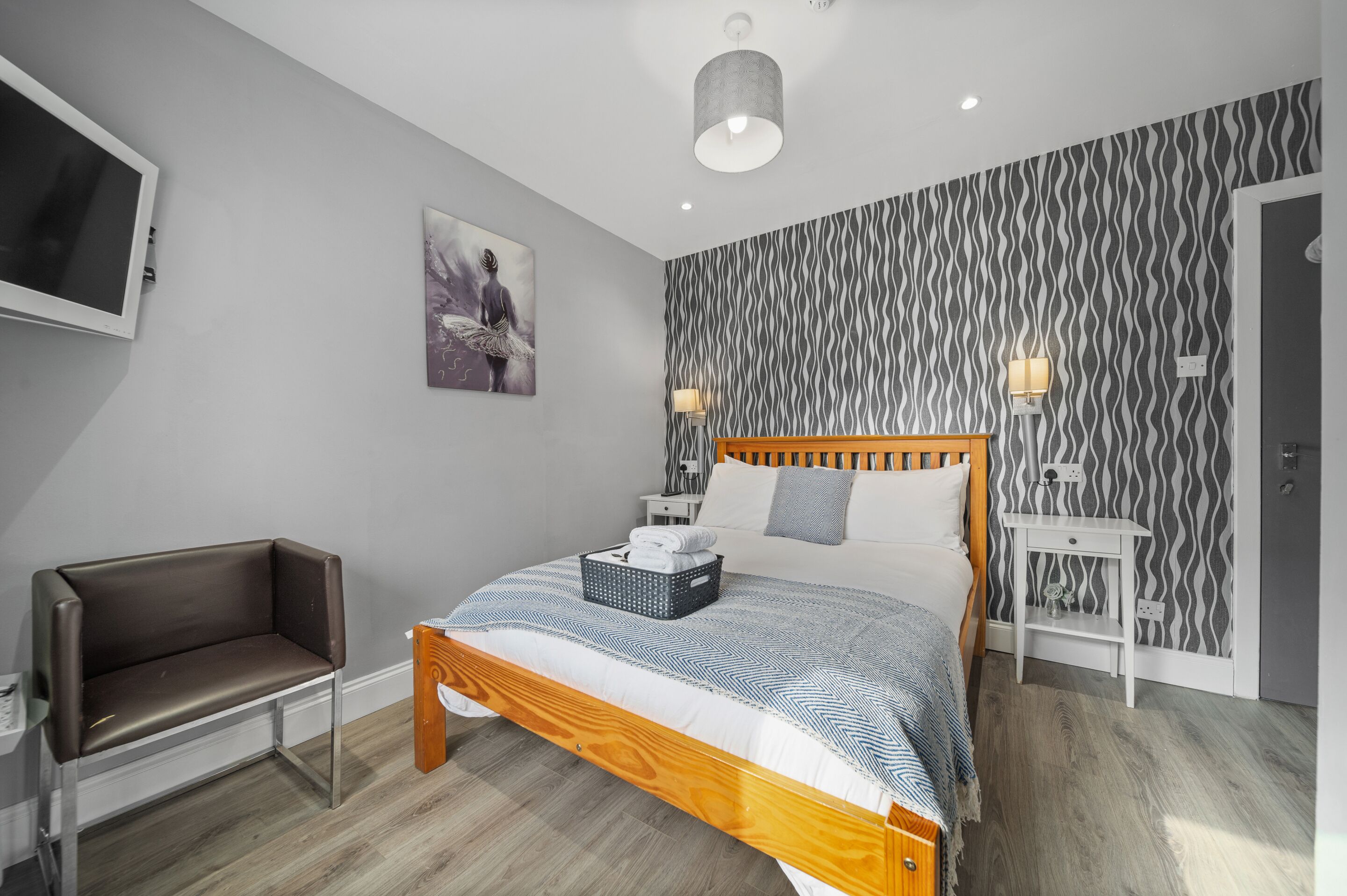 A modern bedroom with a wooden bed, a bench, a TV, and patterned wallpaper.