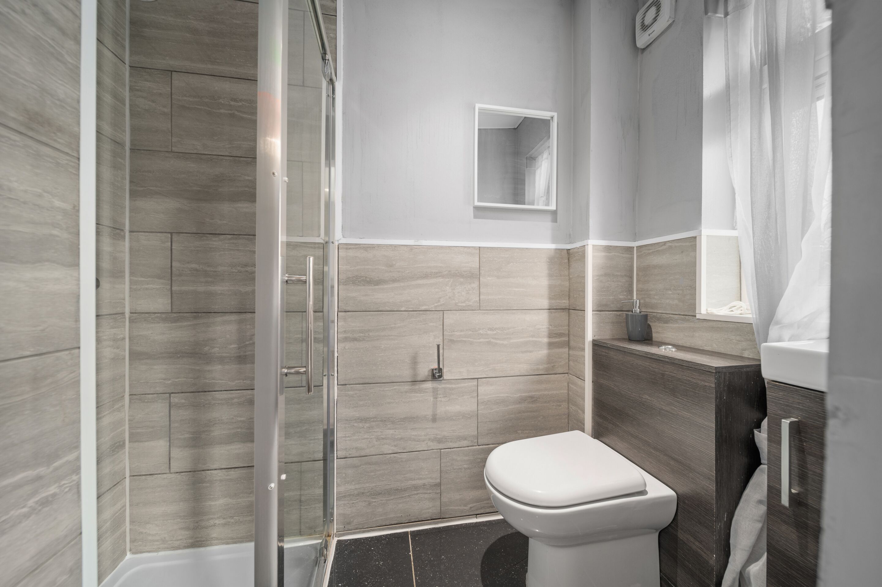 A modern bathroom with a glass shower enclosure, a toilet, and a vanity with a mirror.
