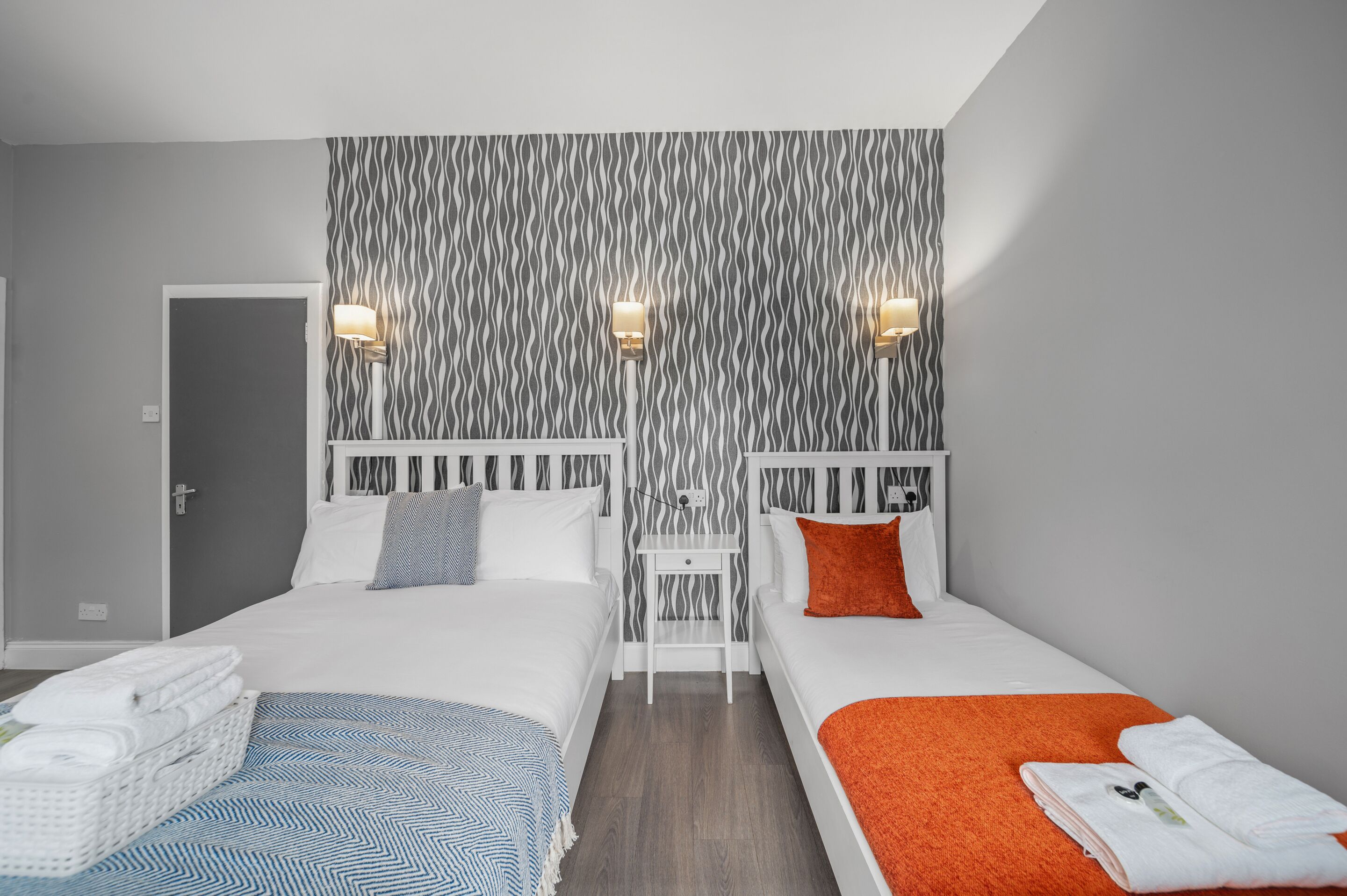 A hotel room with two beds, a small bedside table, and a patterned wallpaper.