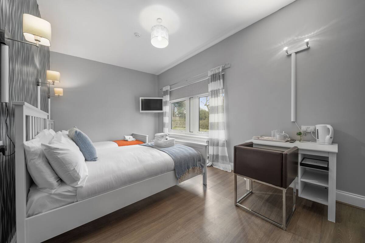 A modern hotel room with a bed, a desk, a chair, a TV, and a window with curtains.