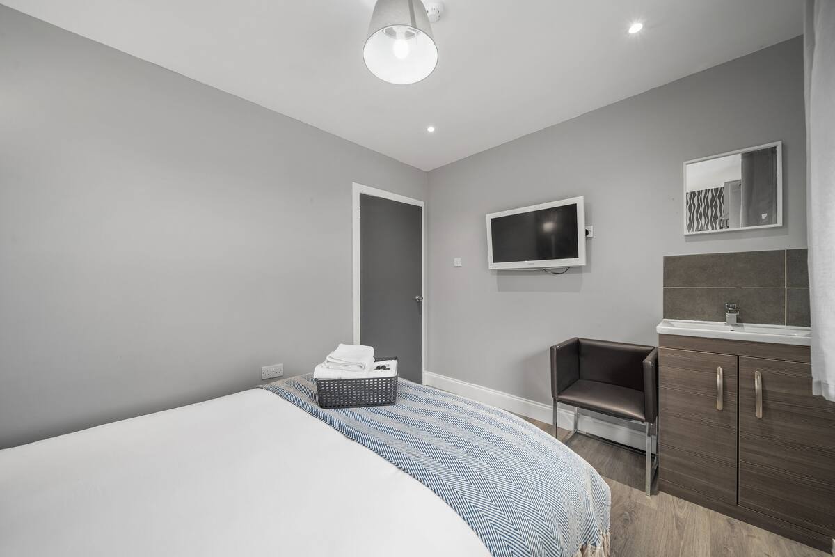 A modern bedroom with a large bed, a bedside table, a TV, and a bathroom with a mirror and sink.