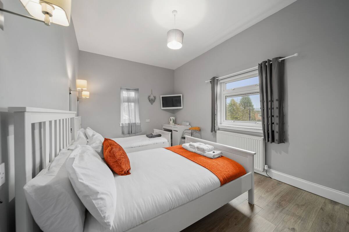 A hotel room with two beds, a desk, a television, and a window with curtains.