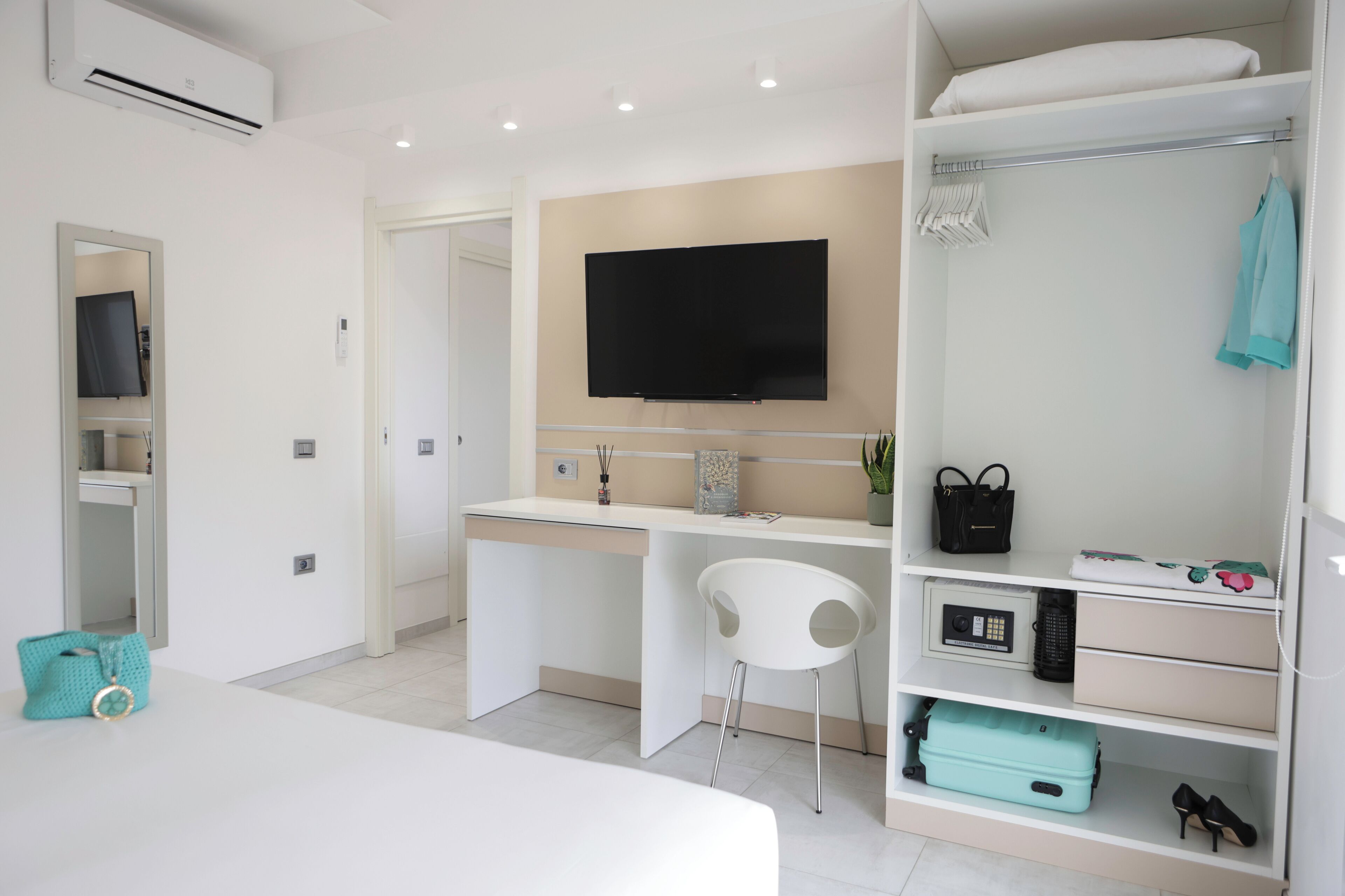 Una habitación de hotel moderna con una cama, un escritorio con silla, un televisor y un vestidor con estantes.