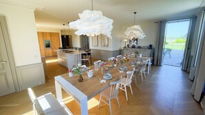 Una cocina moderna con una isla central, un comedor con una larga mesa de madera dispuesta para seis personas, y vistas al exterior a través de amplios ventanales correderas.