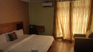 Una habitación de hotel con una cama grande, una silla, una mesita y una ventana con cortinas.
