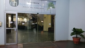 La entrada del hotel Equity Resort, con un vidrio, un mostrador de recepción en el interior y una planta en maceta en el exterior.