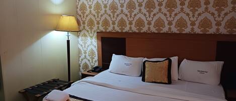 A hotel room with a large bed, a bedside table with a lamp, patterned wallpaper, and a headboard.