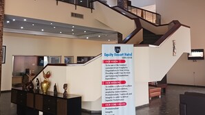 Un vestíbulo amplio con una escalera, una recepción y un cartel que detalla la visión, la misión y los valores fundamentales del hotel.
