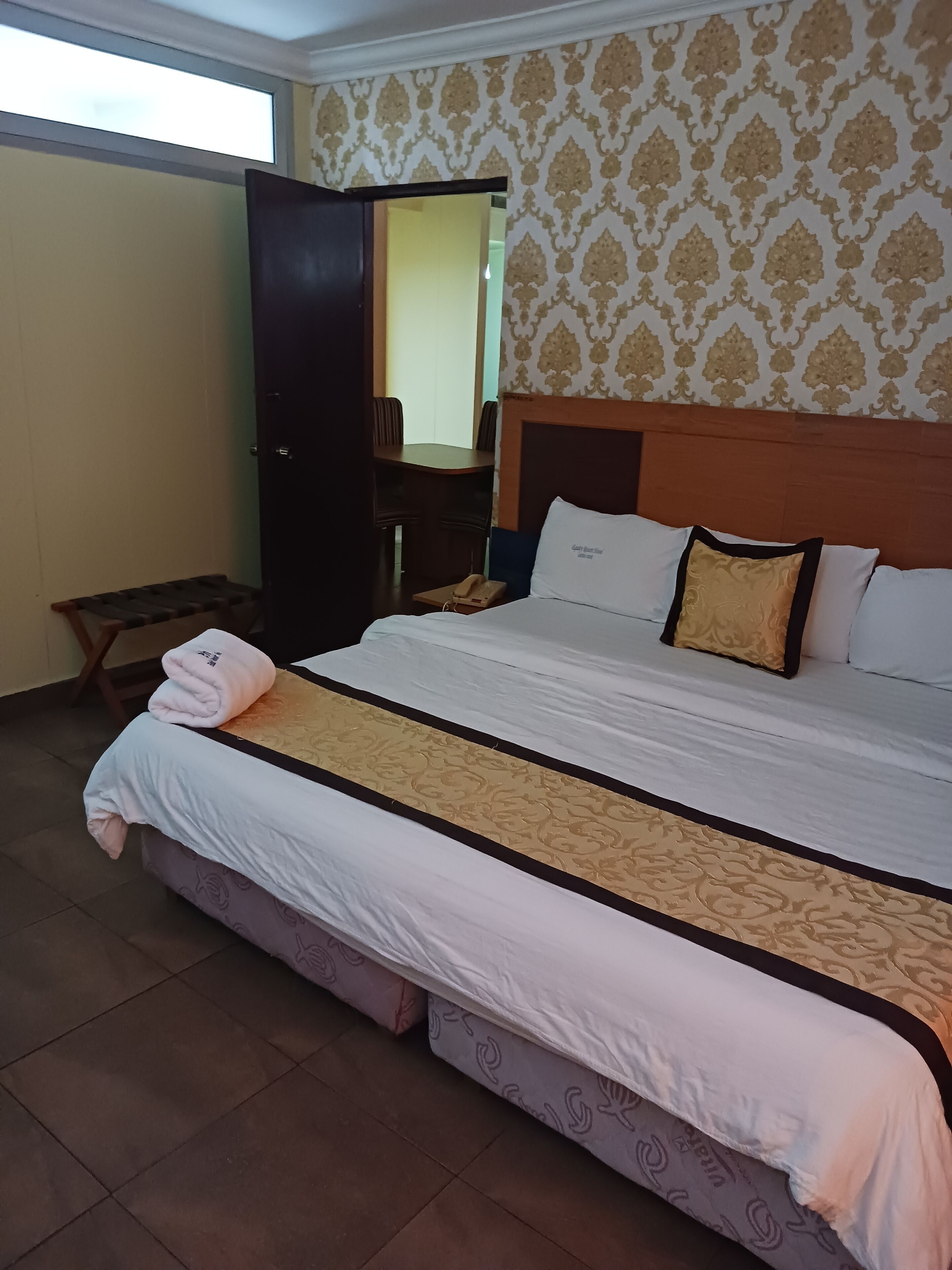 Una habitación de hotel con una cama grande, cabecera de madera, mesita de noche con lámpara y un armario.