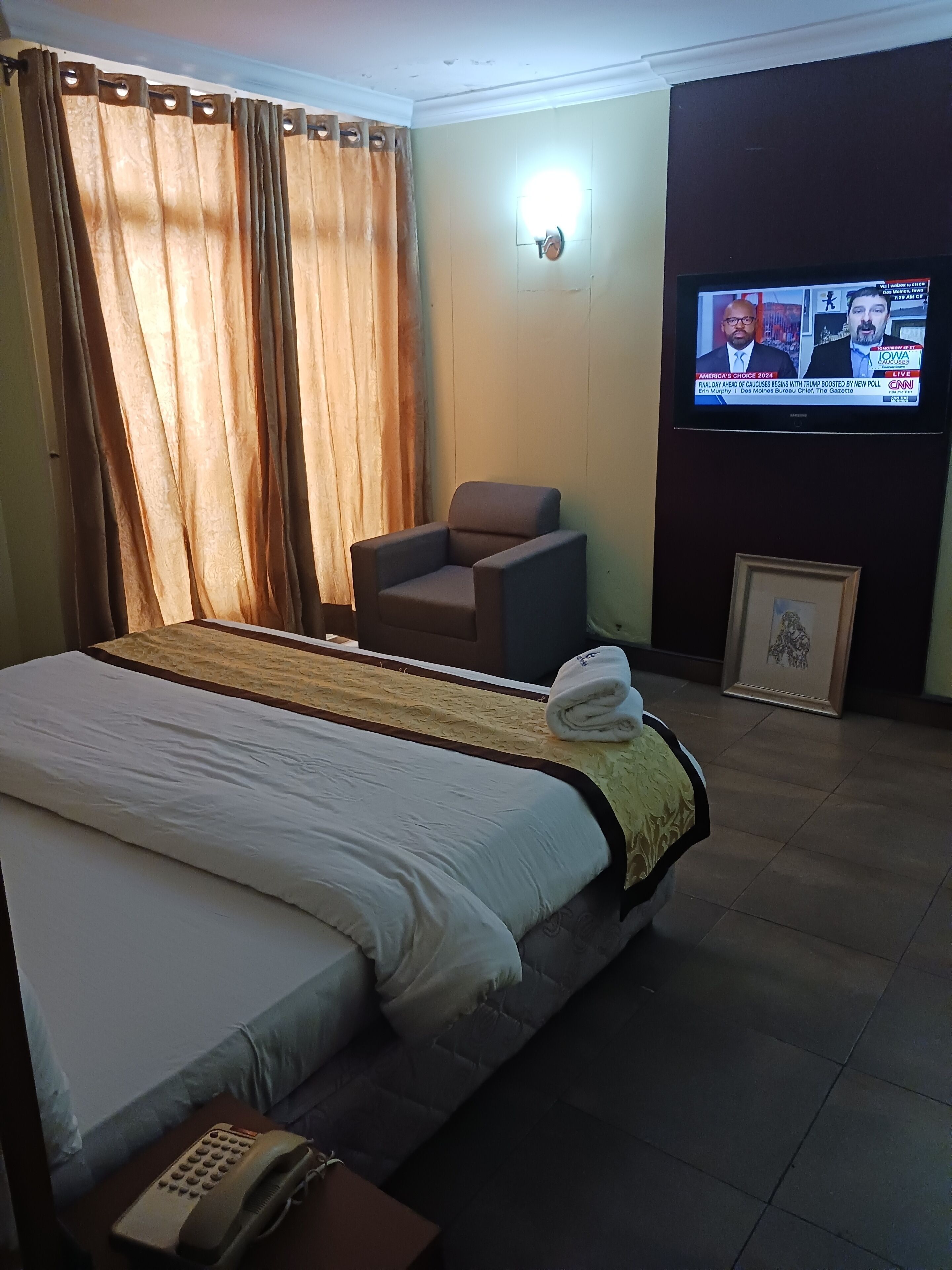 Habitación de hotel con cama, una silla, televisor y un cuadro en la pared.