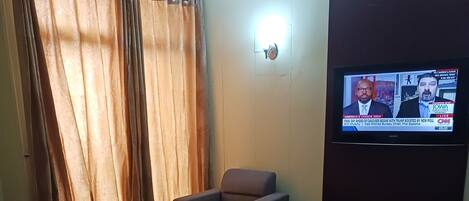 Habitación de hotel con cama, una silla, televisor y un cuadro en la pared.