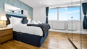 A bedroom with a bed, bedside table, lamp, and a large window with curtains.